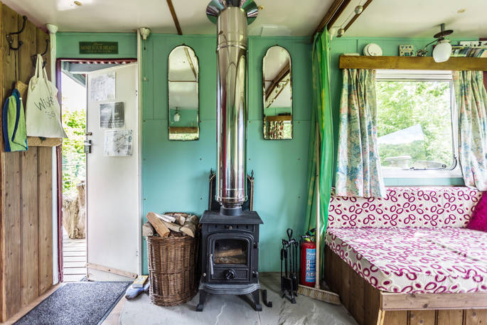 Woodburner inside Van Goff retro caravan  in Powys, Wales with basket of firewood. Cosy cabin interior with doorway leading to outside decking