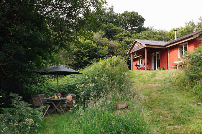 An external view of The Straw Cottage and the hidden woodland dining area in Powys, Wales