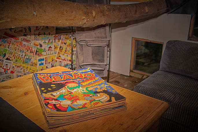 Beano comics on the table with the original artwork hung on the walls in the tree house at Copse Camp 