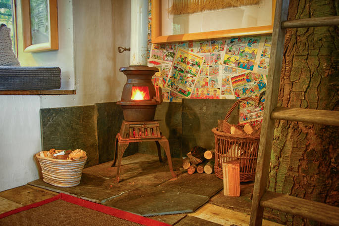 Lit pot belly stove inside the treehouse with baskets of logs beside  