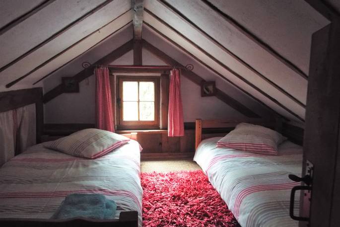 Cosy upstairs bedroom with small window and two comfortable double beds standing alongside a nice cherry rug at Fisherman's Cabin, France