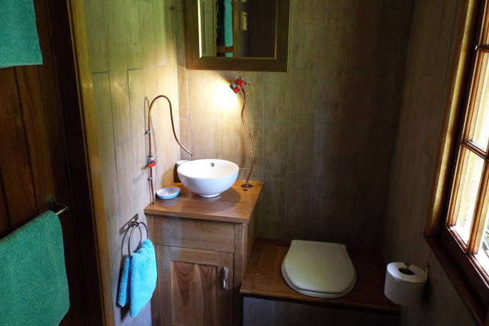 Bathroom at Fisherman's Cabin, with sink and toilet and wooden panels on the wall, and teal towels, Dordogne, France
