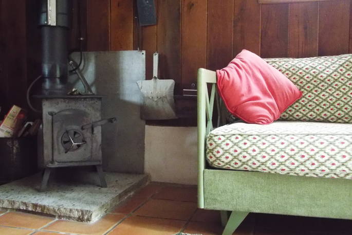 Black wood burner standing next to a mint green patterned couch and pink pollow at Fisherman's Cabin, Dordogne, France