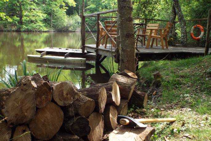 Wood for the log burner laying next to an axe, with the beautiful tranquil lake and al fresco dining area in the background at Fisherman's Cabin, France