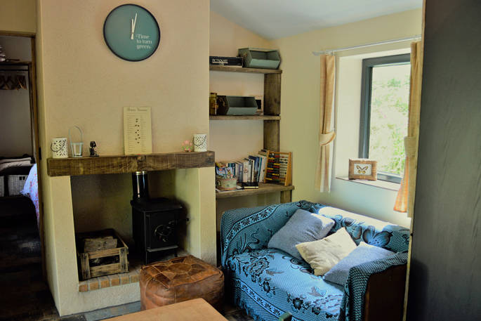 Comfy sofa in the living area with handmade wooden shelves on the walls and log burner next to it inside of GoGreen Cabin in Dordogne 