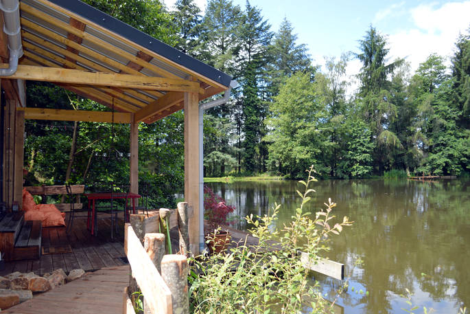 View of GoGreen Cabin from the side next to its own private lake with decking and seating area 