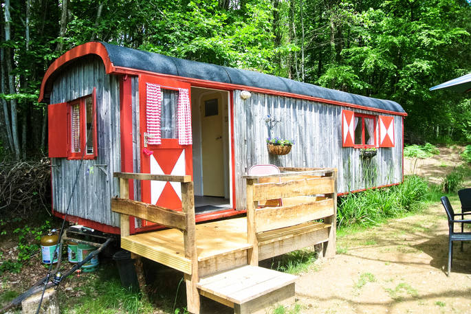 An external view of GoGreen Roulette shepherd's hut with cute curtains and a decking space in Dordogne, France
