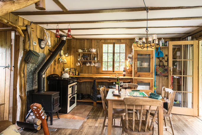 The fully equipped kitchen with dining table and wood burner at Poacher's Cabin in Dordogne, France